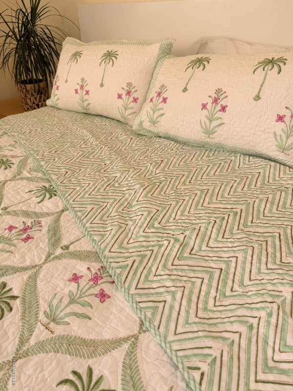 Cotton comforter with two matching pillow cases and floral and palm tree design arranged in arabesques on a queen size bed