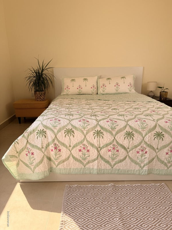 Cotton comforter with two matching pillow cases and floral and palm tree design arranged in arabesques on a queen size bed