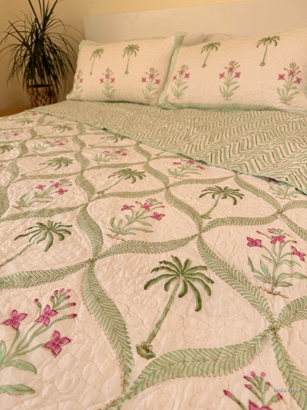 Cotton comforter with two matching pillow cases and floral and palm tree design arranged in arabesques on a queen size bed