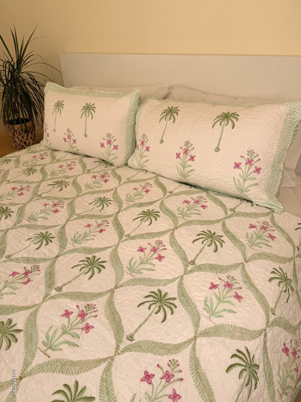 Cotton comforter with two matching pillow cases and floral and palm tree design arranged in arabesques on a queen size bed