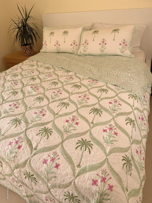 Cotton comforter with two matching pillow cases and floral and palm tree design arranged in arabesques on a queen size bed