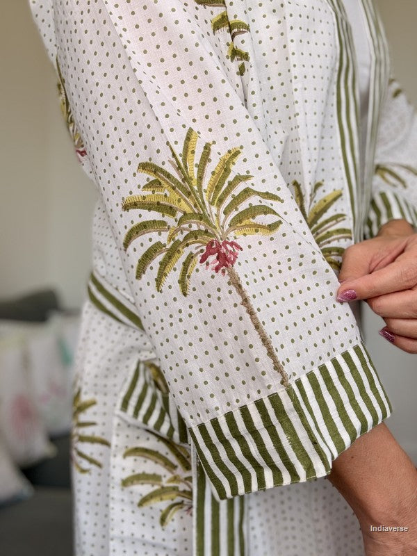 Close-up of a white kurta with green stripes, small gold polka dots, and embroidered green palm tree motifs with pink flower accents, worn by a model.