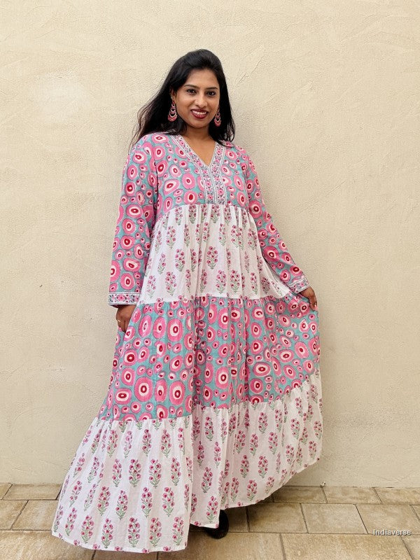 Woman wearing a long cotton dress with circle design and small geometrical floral print standing against a beige wall
