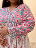Woman wearing a long cotton dress with circle design and small geometrical floral print standing against a beige wall