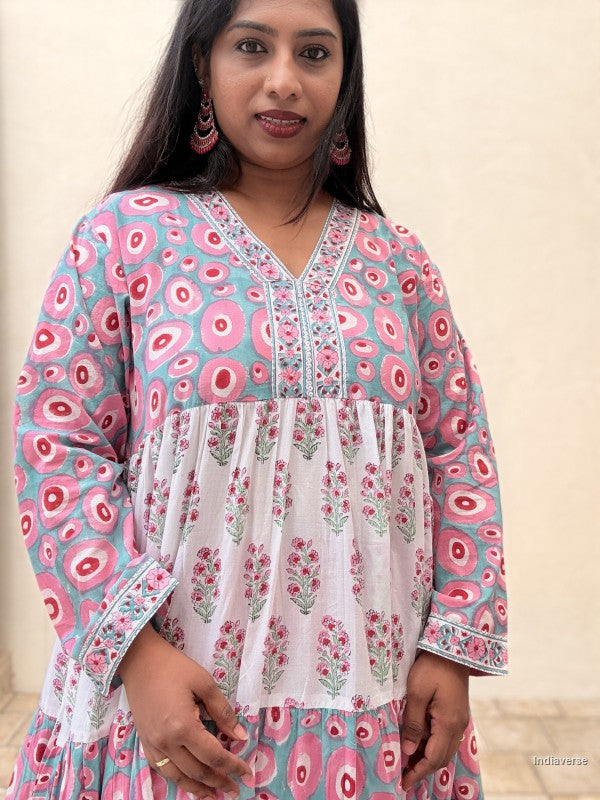 Woman wearing a long cotton dress with circle design and small geometrical floral print standing against a beige wall