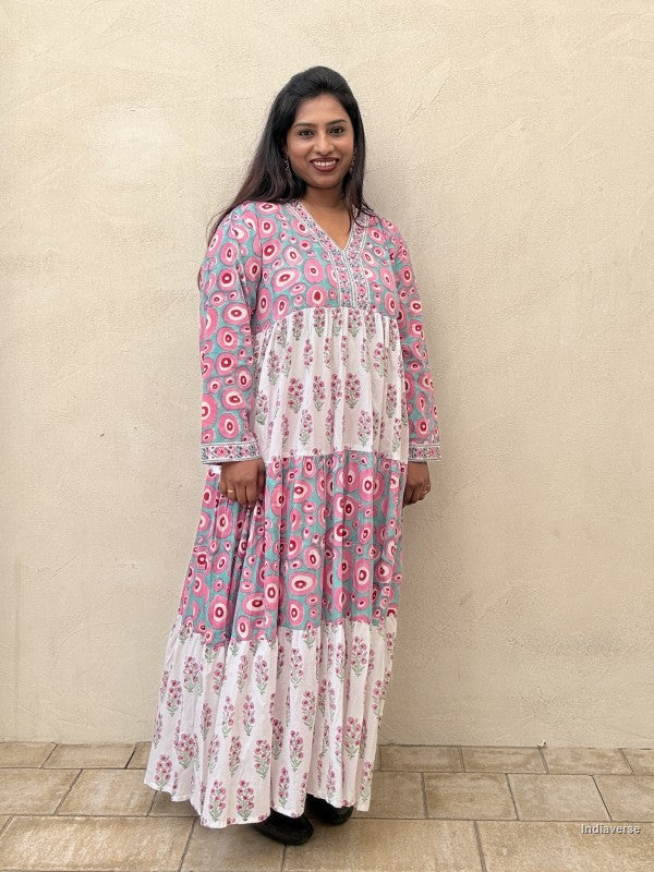 Woman wearing a long cotton dress with circle design and small geometrical floral print standing against a beige wall