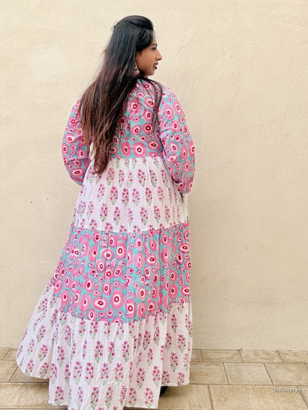 Woman wearing a long cotton dress with circle design and small geometrical floral print standing against a beige wall
