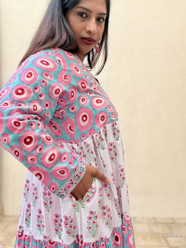 Woman wearing a long cotton dress with circle design and small geometrical floral print standing against a beige wall