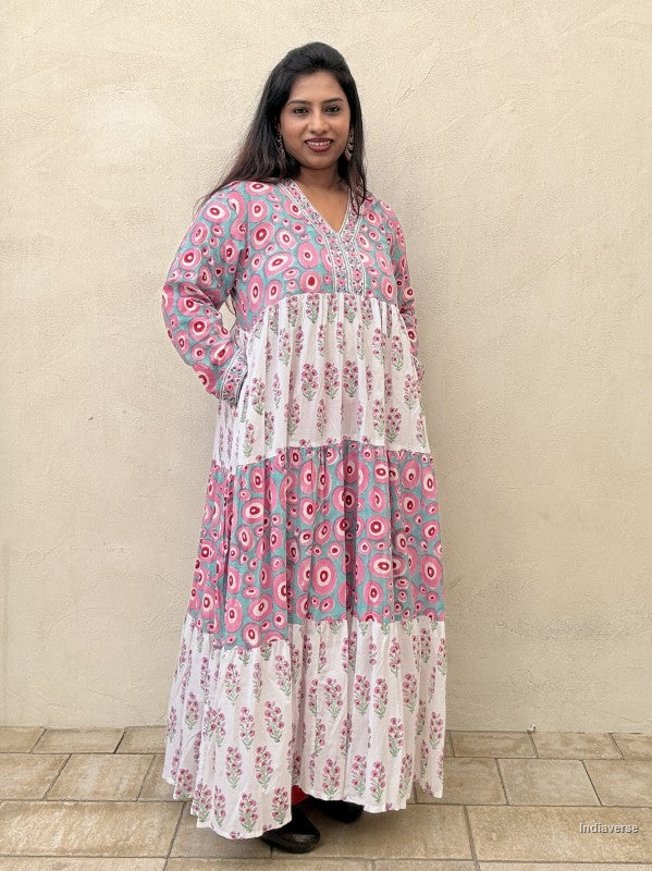 Woman wearing a long cotton dress with circle design and small geometrical floral print standing against a beige wall