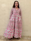 Woman wearing a long cotton maxi dress with traditional small flower design and big pink poppy motif standing against a beige wall