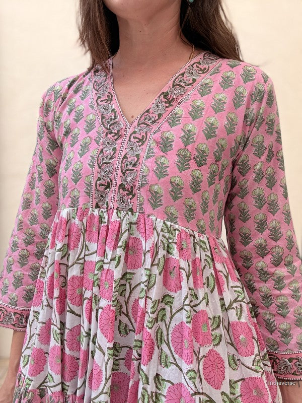 Close up of a woman wearing a long cotton maxi dress with traditional small flower design and big pink poppy motif standing against a beige wall