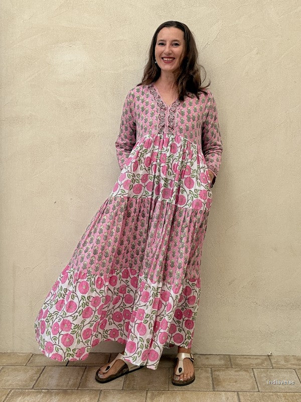 Woman wearing a long cotton maxi dress with traditional small flower design and big pink poppy motif standing against a beige wall