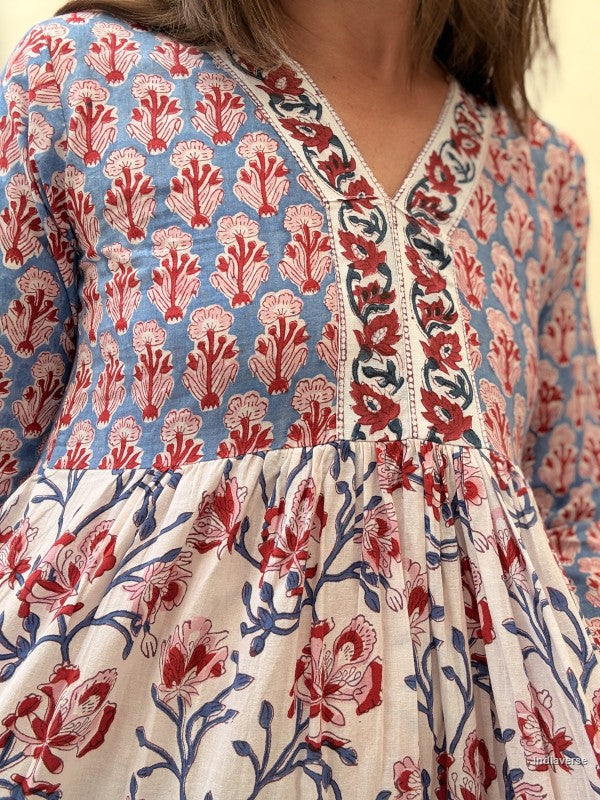 A close-up of a woman wearing a printed dress with a blue upper section featuring red and pink floral motifs, and a cream lower section with red and blue floral patterns.