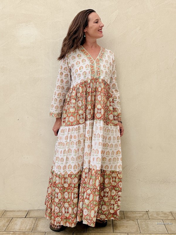 A Woman wearing a long maxi dress made from cotton with floral and palm tree print motif standing against a beige wall