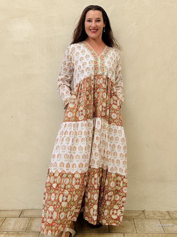 A Woman wearing a long maxi dress made from cotton with floral and palm tree print motif standing against a beige wall