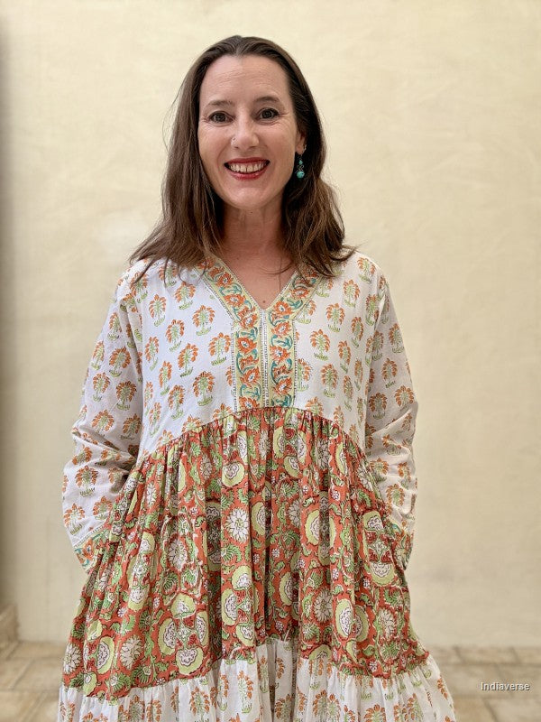 A Woman wearing a long maxi dress made from cotton with floral and palm tree print motif standing against a beige wall