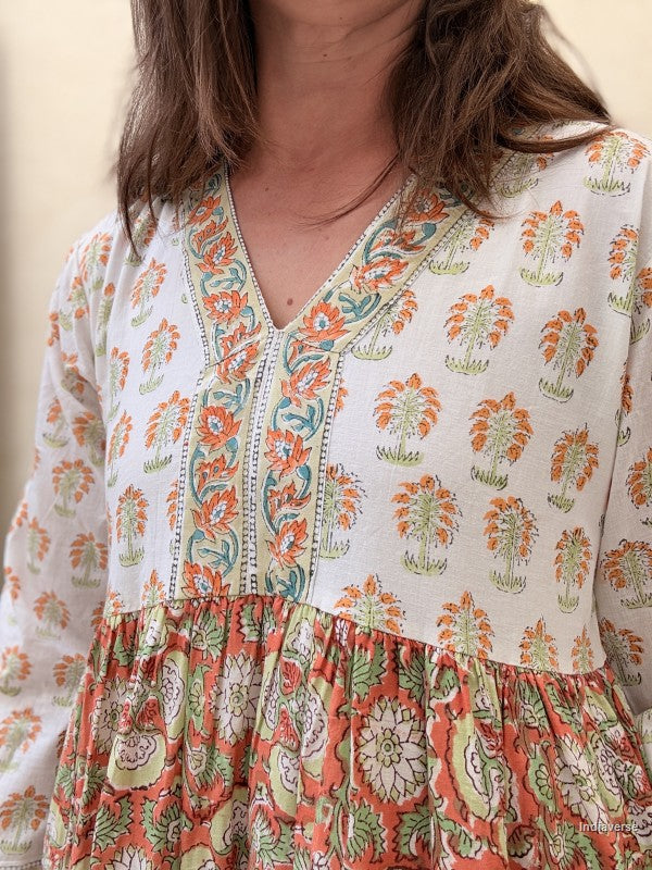 Close up of a Woman wearing a long maxi dress made from cotton with floral and palm tree print motif standing against a beige wall
