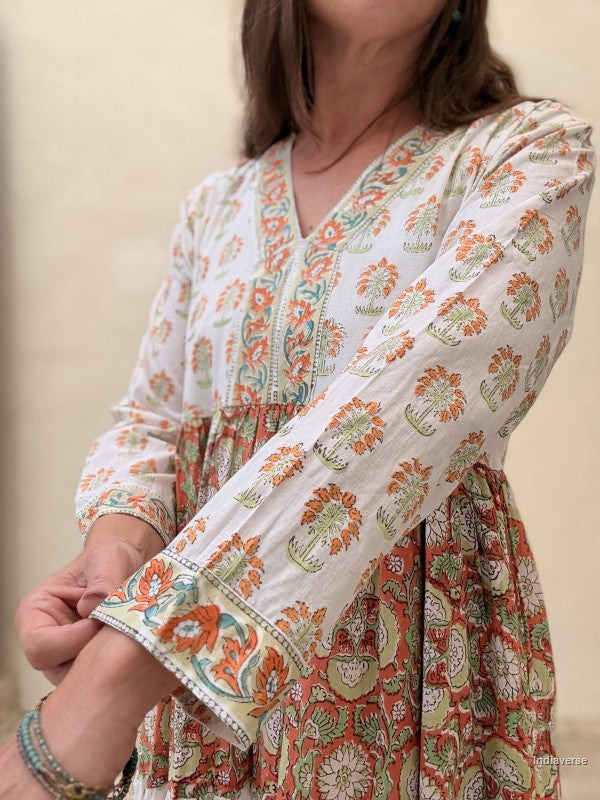 Close up of a woman wearing a long maxi dress made from cotton with floral and palm tree print motif standing against a beige wall