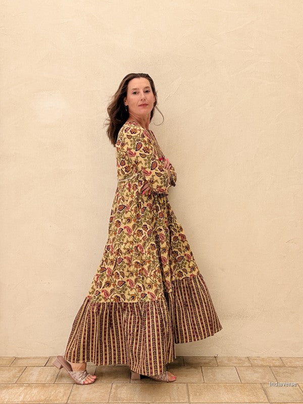 Woman wearing a long, patterned dress against a beige wall.