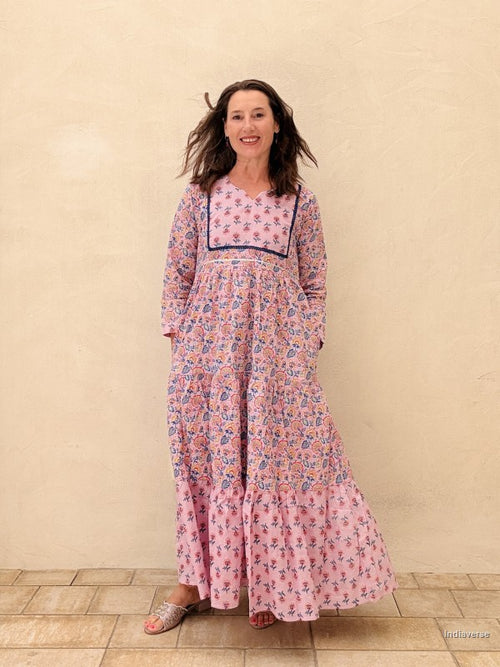 Woman wearing a pink floral dress standing against a beige wall.