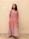 Woman wearing a long floral dress against a beige wall.