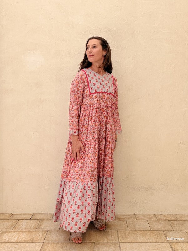 Woman wearing a long floral dress against a beige wall.