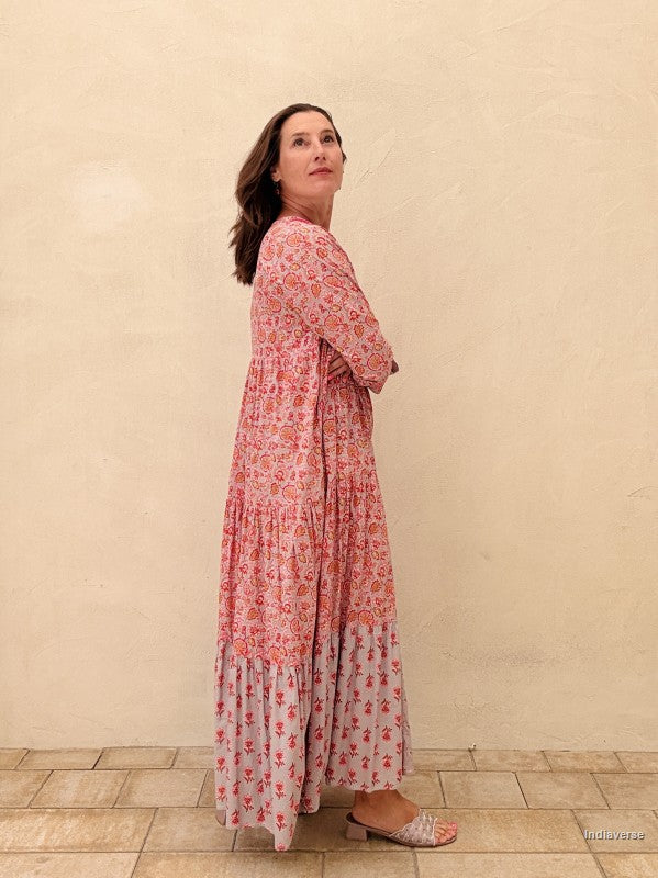 Woman wearing a long floral dress against a beige wall.