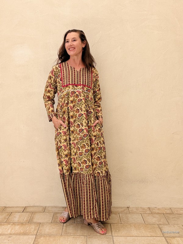 Woman wearing a long, patterned dress standing against a plain wall.