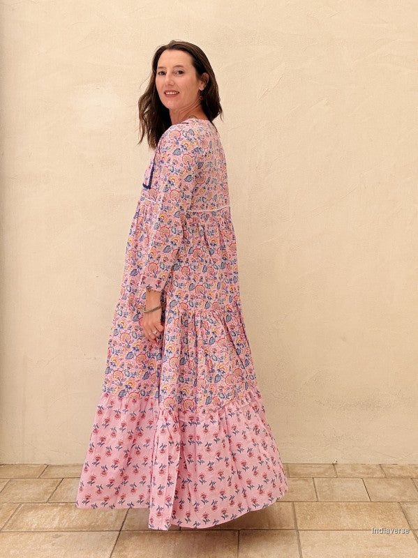 Woman wearing a long floral dress against a beige wall.