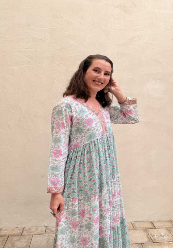 Woman standing in front of a beige wall wearing a long cotton dress with floral design in turquoise hues