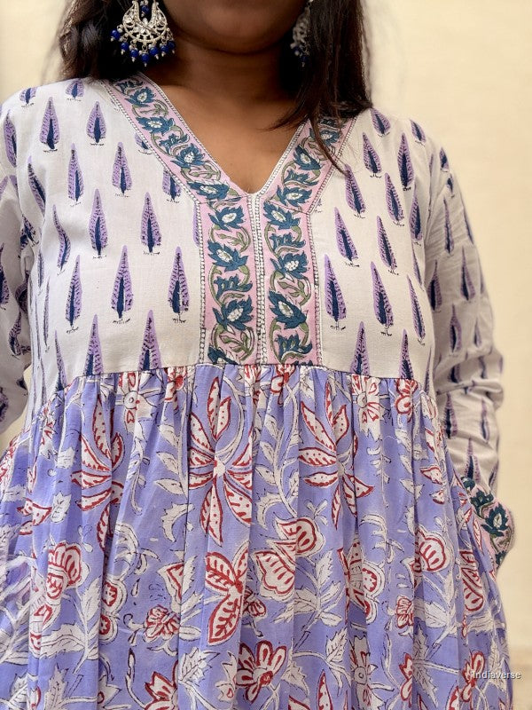 Close up of a woman standing in front of a beige wall wearing a beautiful long cotton dress with floral and cypress prints in aquamarine blue tones
