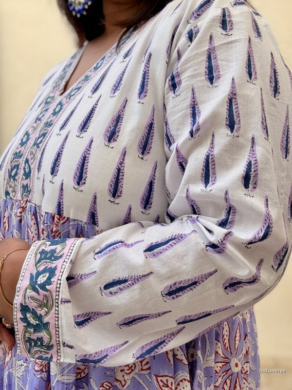 Close up of a woman standing in front of a beige wall wearing a beautiful long cotton dress with floral and cypress prints in aquamarine blue tones