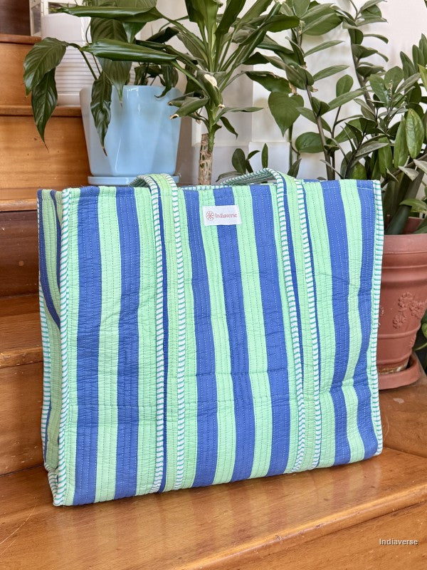 Blue and green striped bag on a wooden surface with plants in the background
