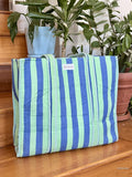 Blue and green striped bag on a wooden surface with plants in the background