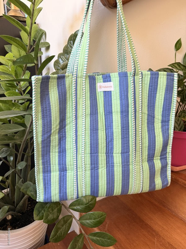 quilted tote bag hanging from a handle bar with green and blue stripes