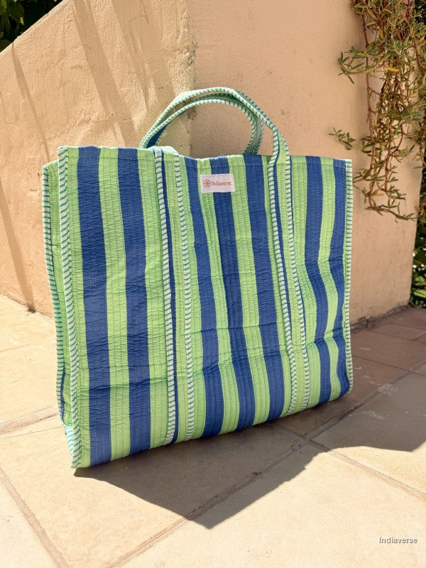 green and blue striped tote bag sitting in front of a beige wall