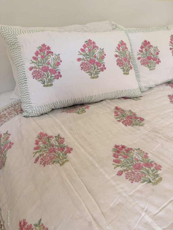 Close up of two pillowcases with pink floral design arranged on a quilt with the same floral pattern on a bed