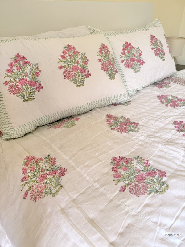 Close up of a pink and white floral quilt spread out on a white double bed with two matching pillowcases in a styled bedroom