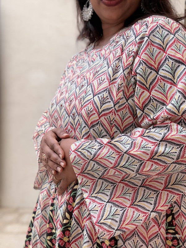 A close-up of a woman wearing a loose, long-sleeve kurta with a geometric leaf pattern in pink, black, and beige, paired with a floral skirt.