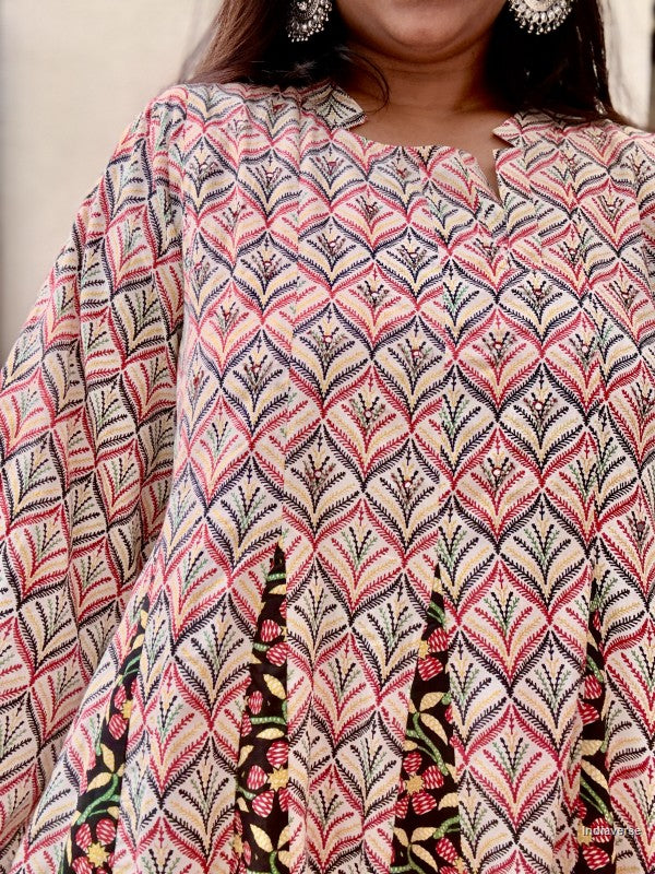 A close-up of a woman wearing a loose, long-sleeve tunic top with a detailed geometric and floral block print in pink, red, green, and beige.