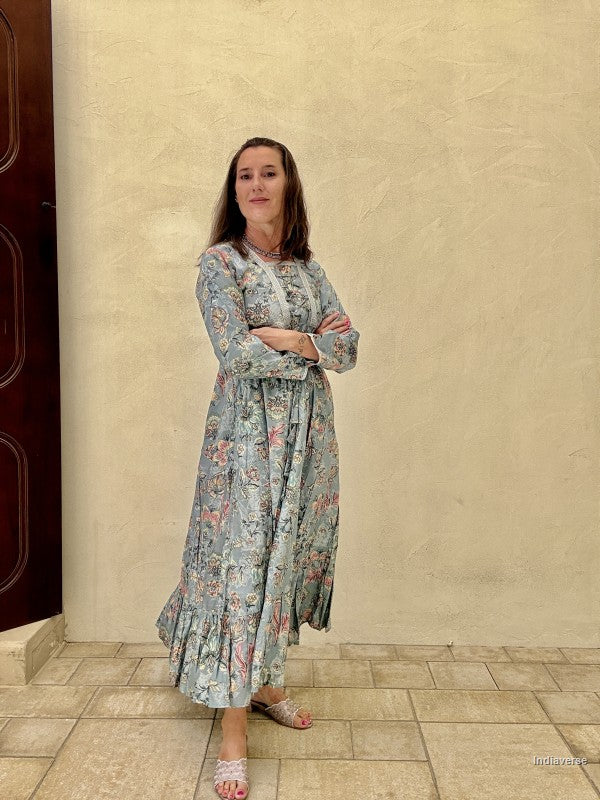 Woman in a floral dress standing against a beige wall.