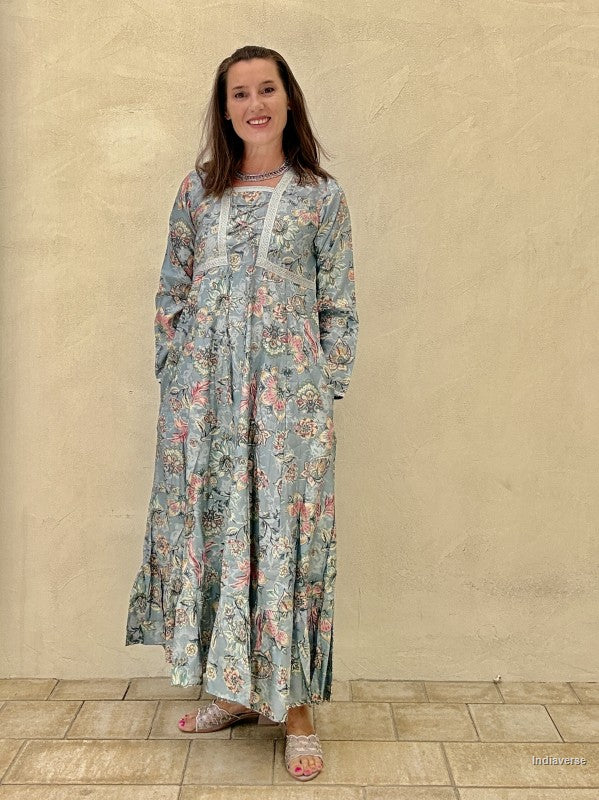 Woman wearing a long floral dress against a beige wall.