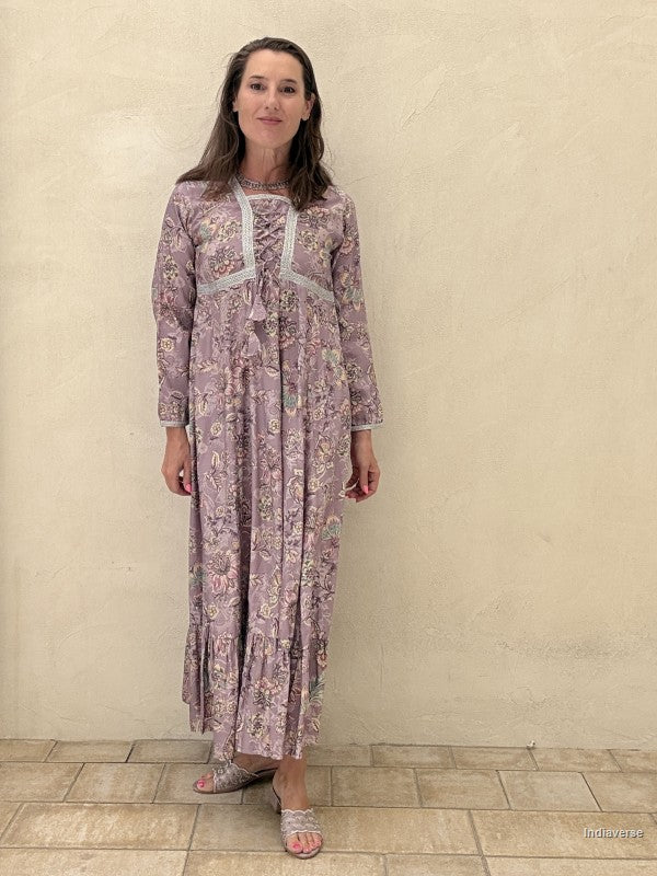 Woman wearing a long floral dress against a beige wall.