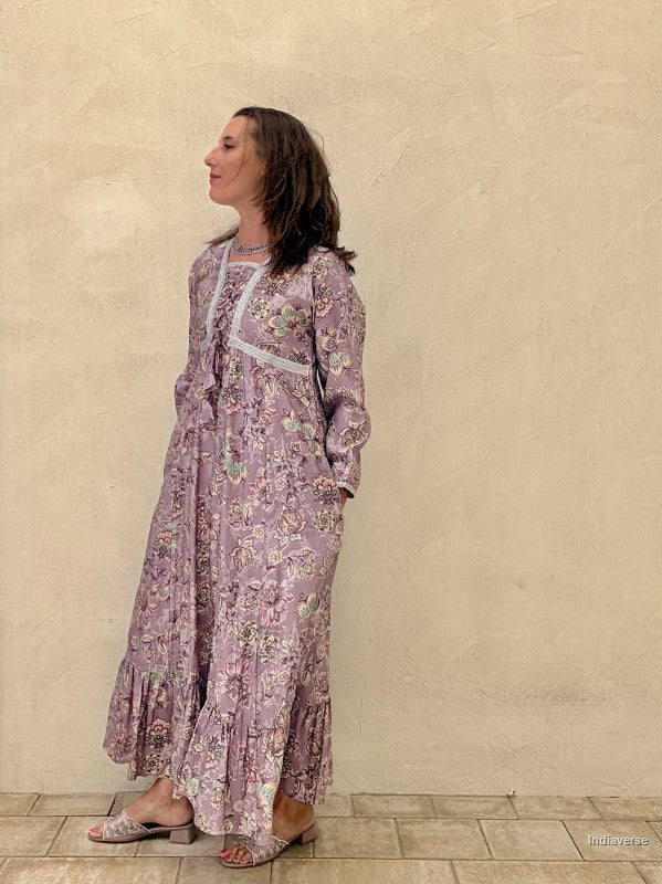 Woman wearing a long floral dress against a beige wall.