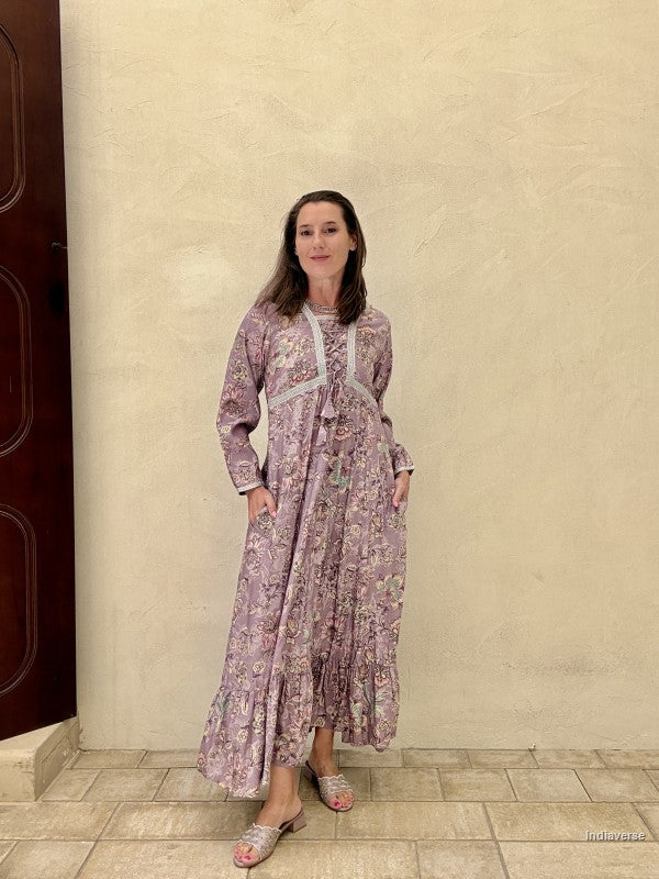 Woman in a long floral dress standing against a beige wall.