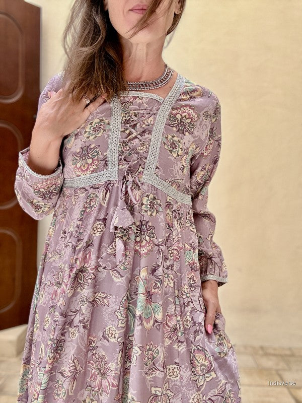 Woman wearing a floral dress with intricate details against a beige wall.
