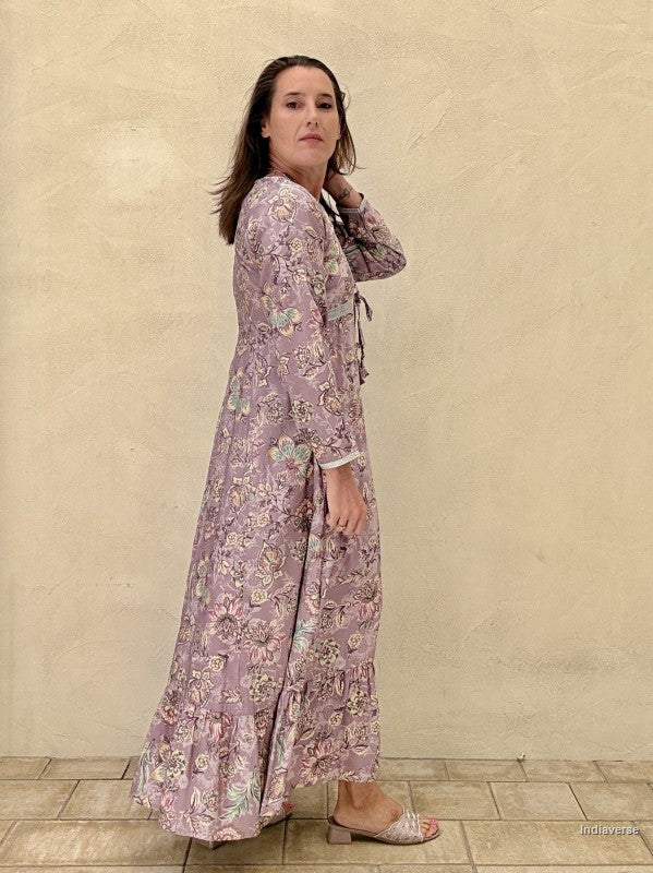Woman wearing a long floral dress against a beige wall.