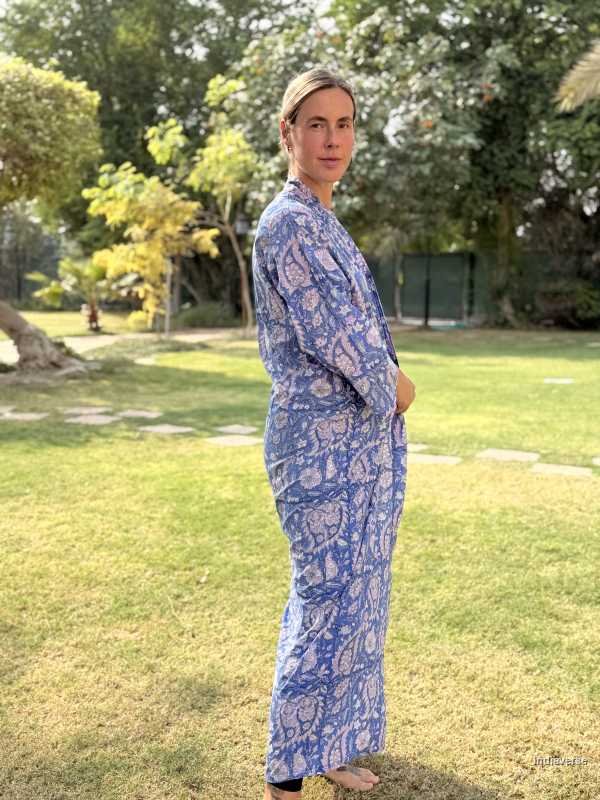 Person wearing a blue patterned dress standing in a grassy area with trees in the background