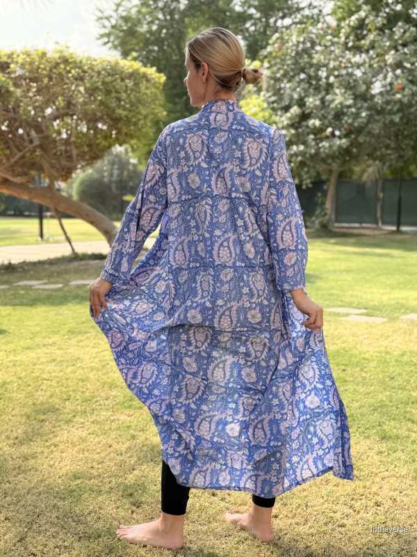 Woman wearing a blue patterned outfit standing in a grassy area with trees.