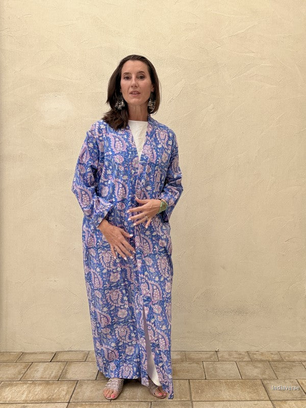 Woman wearing a blue patterned dress standing against a beige wall.